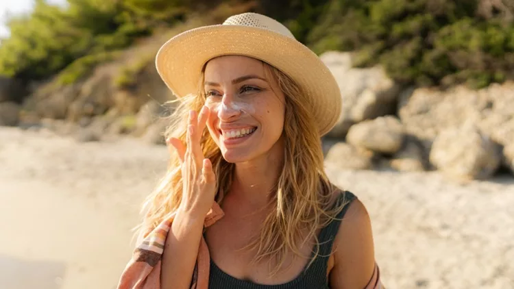 Χαρούμενη γυναίκα που βάζει αντηλιακό στο πρόσωπό της - καλοκαίρι στην παραλία