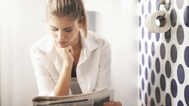 Γυναίκα με πρόβλημα δυσκοιλιότητας που διαβάζει εφημερίδα στην τουαλέτα