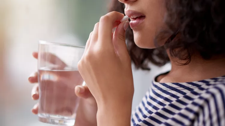 γυναίκα κρατάει ποτήρι με νερό και παίρνει συμπληρώματα διατροφής