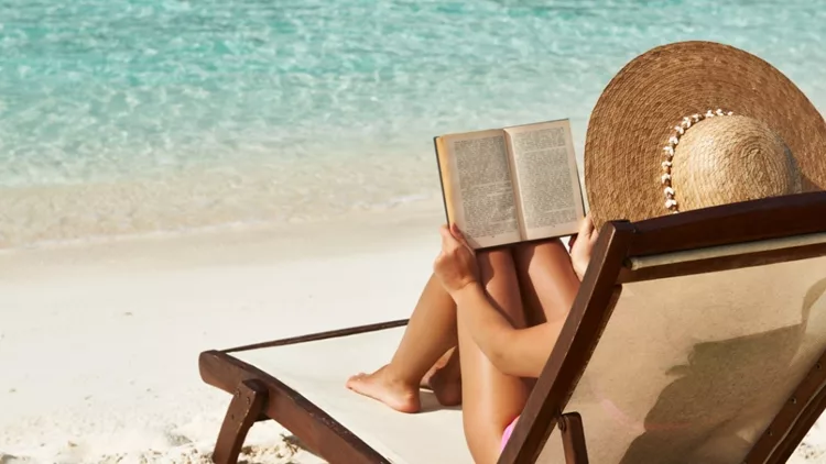 Γυναίκα που διαβάζει το βιβλίο της στην παραλία στις καλοκαιρινές διακοπές