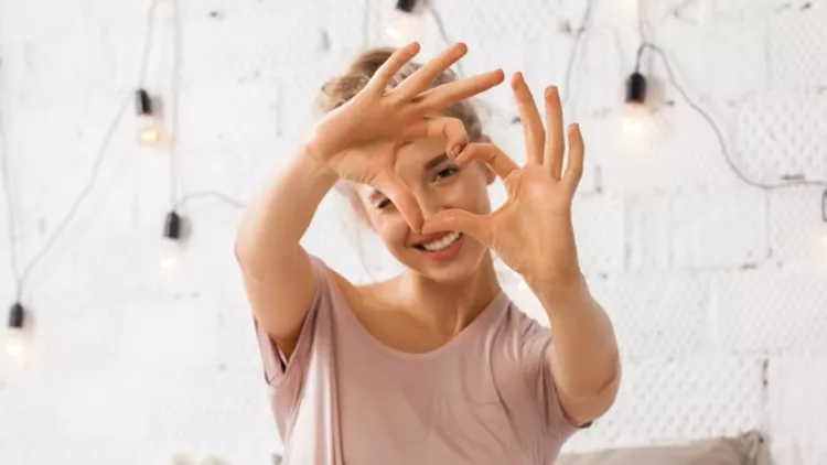 woman-sitting-on-bed-and-shows-gesture-heart-with-fingers-picture-id885774646