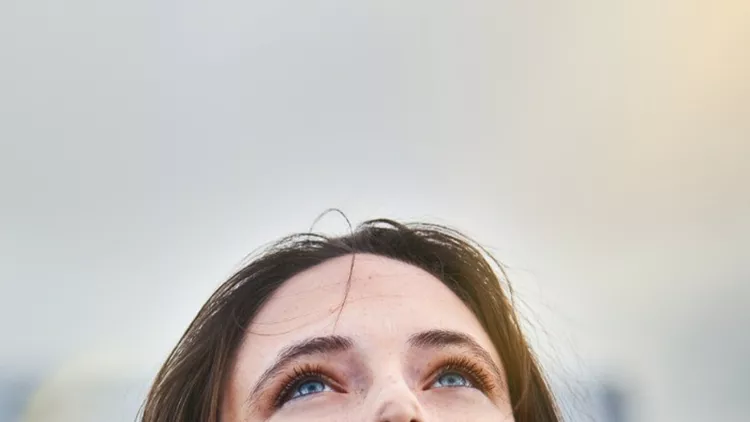 young-woman-looks-hopeful-as-she-raises-her-eyes-towards-the-sky-picture-id911330238