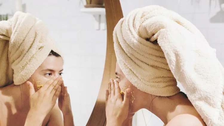 young-happy-woman-in-towel-applying-organic-face-scrub-and-looking-at-picture-id1126244497