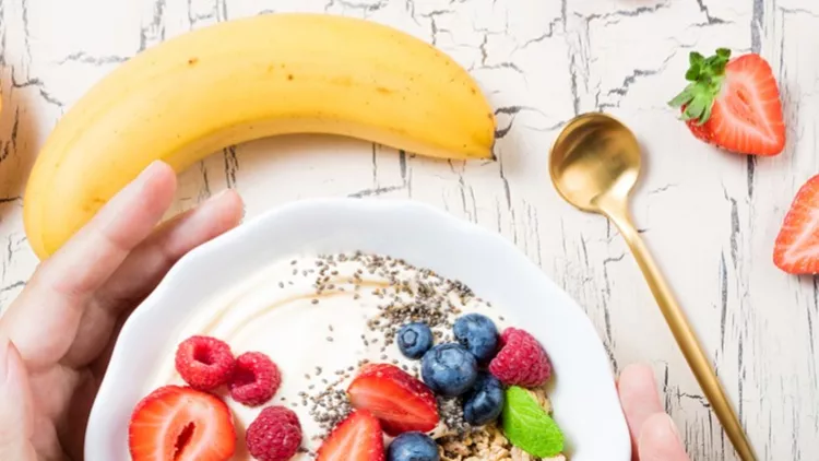 womens-hands-holding-granola-with-berries-fruits-yoghurt-and-coffee-picture-id1049372582