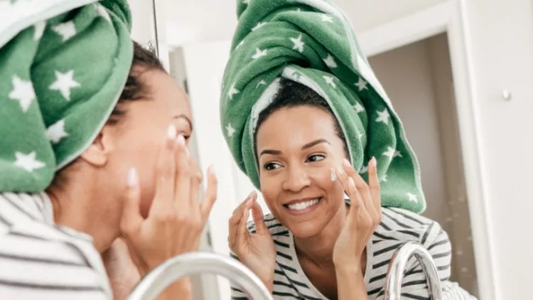 woman-with-towel-applying-face-cream-picture-id933373874