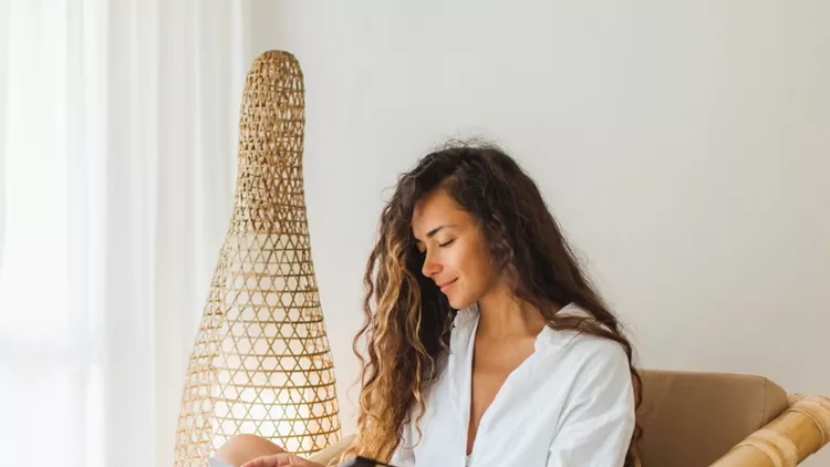 young-brunette-woman-sitting-in-wooden-bamboo-chair-indoors-and-book-picture-id1159560280