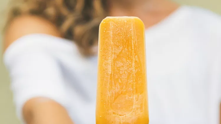 mango-citrus-ice-cream-popsicle-in-woman-hand-square-crop-picture-id1129058107