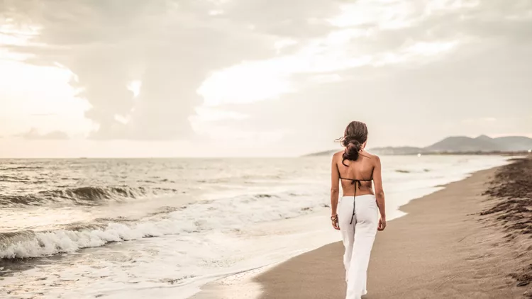 Young woman walking alone on sand by the sea.