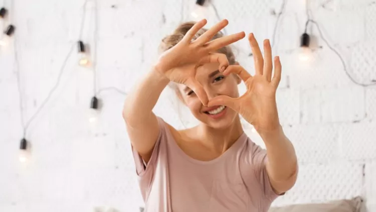 woman-sitting-on-bed-and-shows-gesture-heart-with-fingers-picture-id885774646