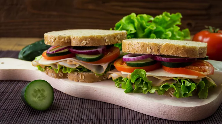Sandwich with ham, cheese, tomatoes, lettuce, cucumbers and onions on a wooden background