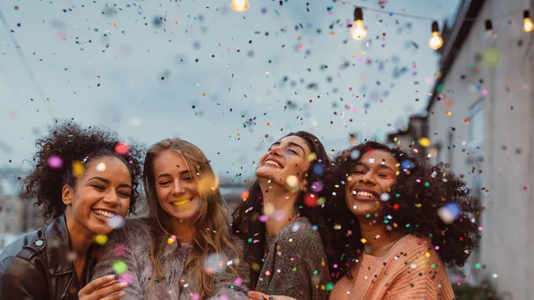 Four beautiful women standing at a terrace under confetti.