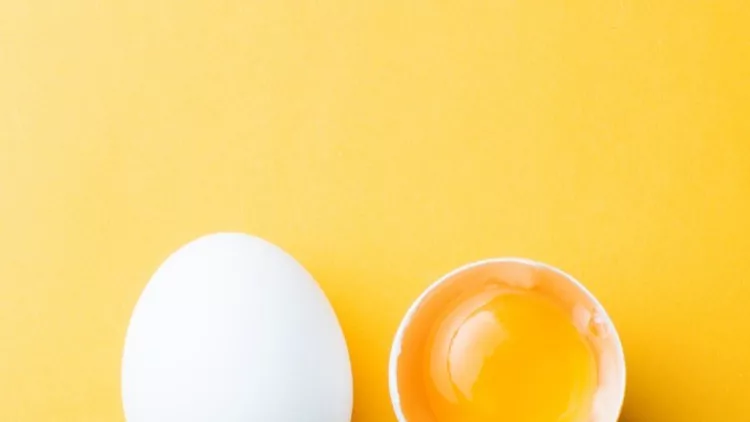 white-egg-and-egg-yolk-on-the-yellow-background-topview-picture-id905347554