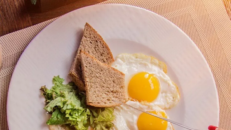 woman-eating-fried-eggs-with-toasts-and-coffee-picture-id998337352