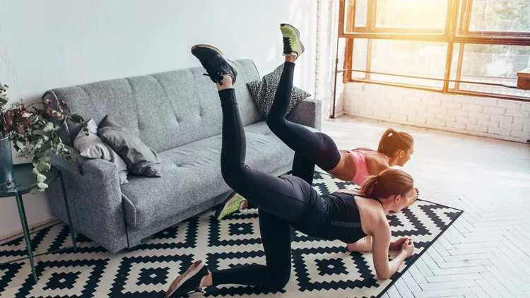 Two sportive female friends doing butt toning exercise performing donkey kicks at home