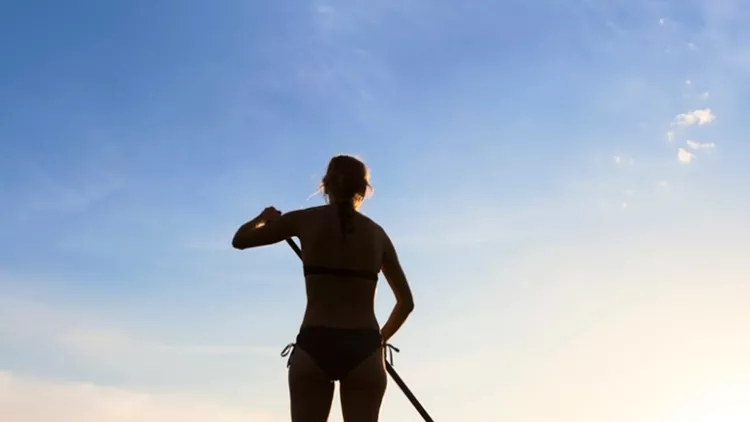 girl-stand-up-paddle-boarding-on-quiet-sea-sunset-picture-id629170142