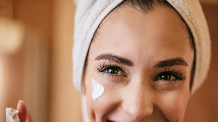 young-happy-woman-applying-moisturizer-on-her-face-in-the-bathroom-picture-id1208515511 (1)
