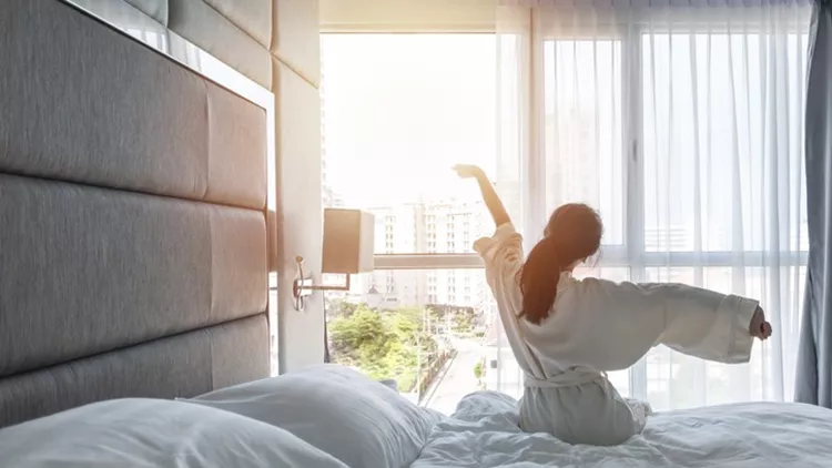 Hotel room comfort with good sleep easy relaxation lifestyle of Asian girl on bed have a nice day morning waking up, taking some rest, lazily relaxing in guest bedroom in city hotel