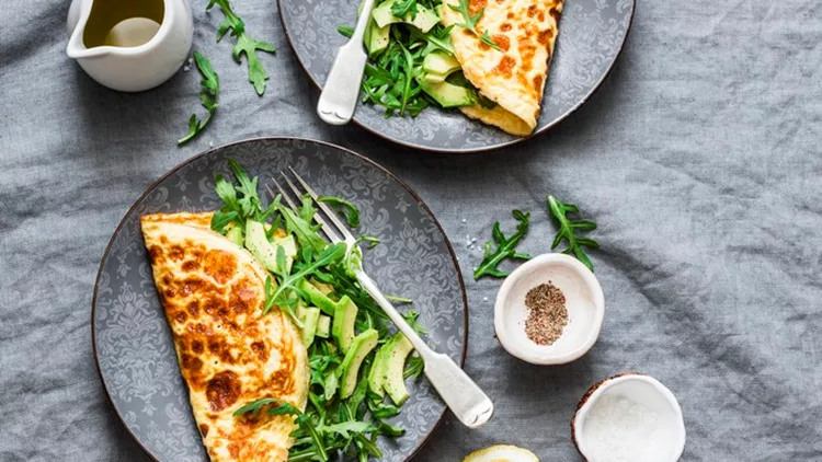 Omelette with cream cheese, arugula and avocado salad on a grey background, top view. Healthy breakfast or diet lunch