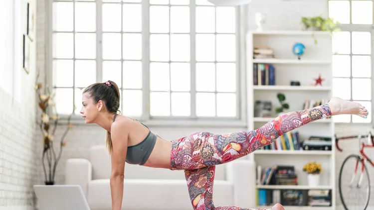 Young sporty attractive woman practicing yoga, doing Donkey Kick exercise in front of her laptop