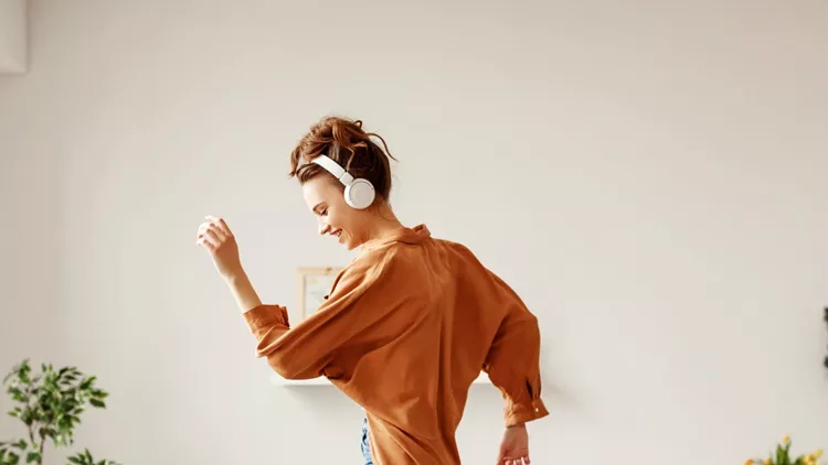 cheerful-woman-listening-to-music-and-dancing-on-soft-couch-at-home-picture-id1219638428