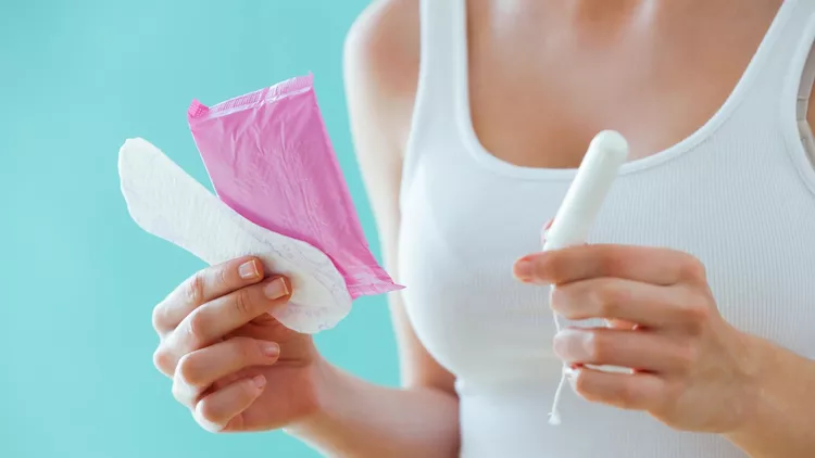 Young woman with a menstrual compress and a tampon on blue background.