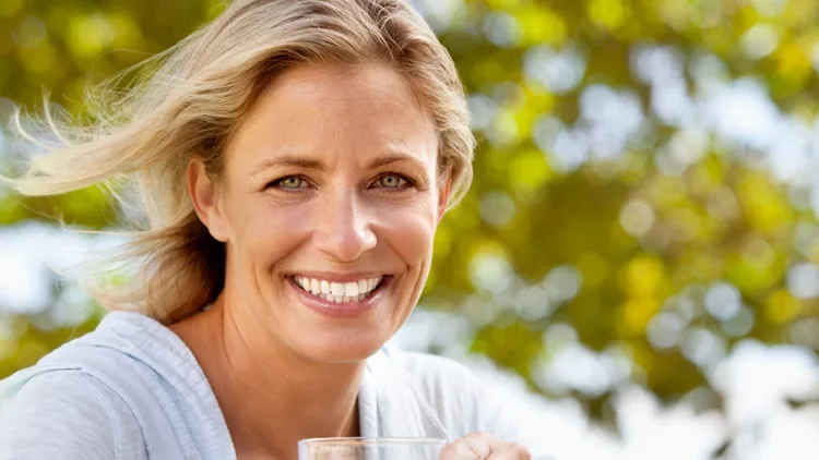 smiling-mature-woman-with-orange-juice-at-breakfast-table-outdoors-picture-id124206631