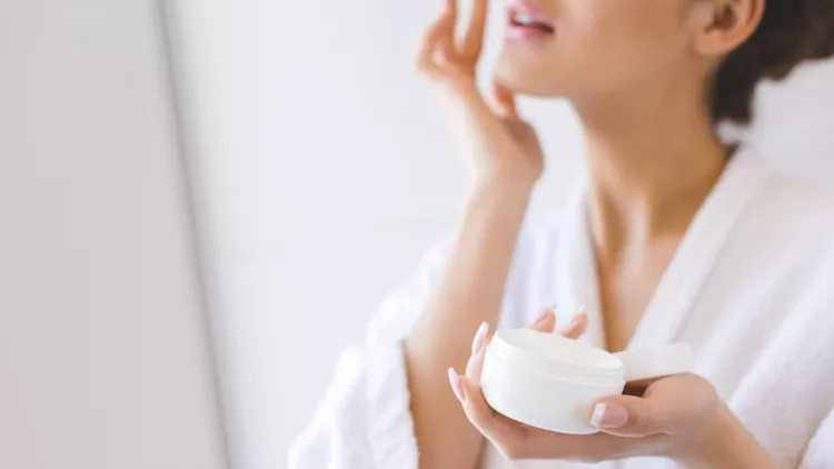 cropped-shot-of-beautiful-woman-in-bathrobe-applying-face-cream-picture-id923660962