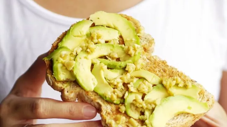 woman-hand-show-eating-avocado-bread-cheese-toast-white-tshirt-picture-id891931888