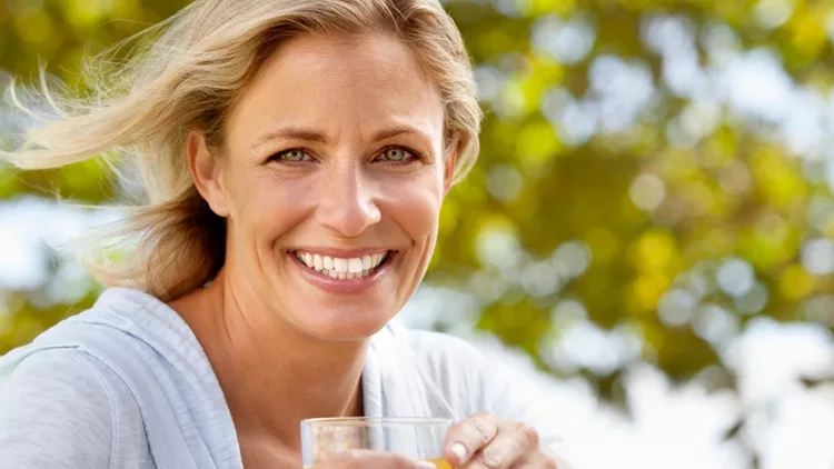 smiling-mature-woman-with-orange-juice-at-breakfast-table-outdoors-picture-id124206631