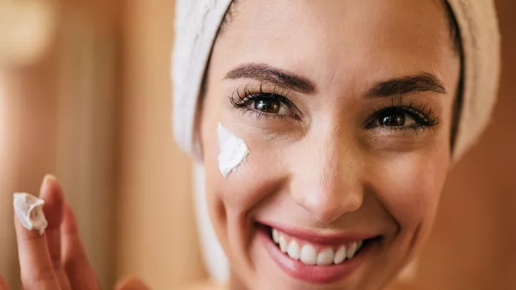 young-happy-woman-applying-moisturizer-on-her-face-in-the-bathroom-picture-id1208515511 (1)