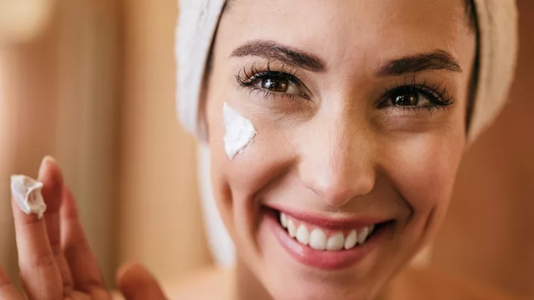 young-happy-woman-applying-moisturizer-on-her-face-in-the-bathroom-picture-id1208515511 (1)